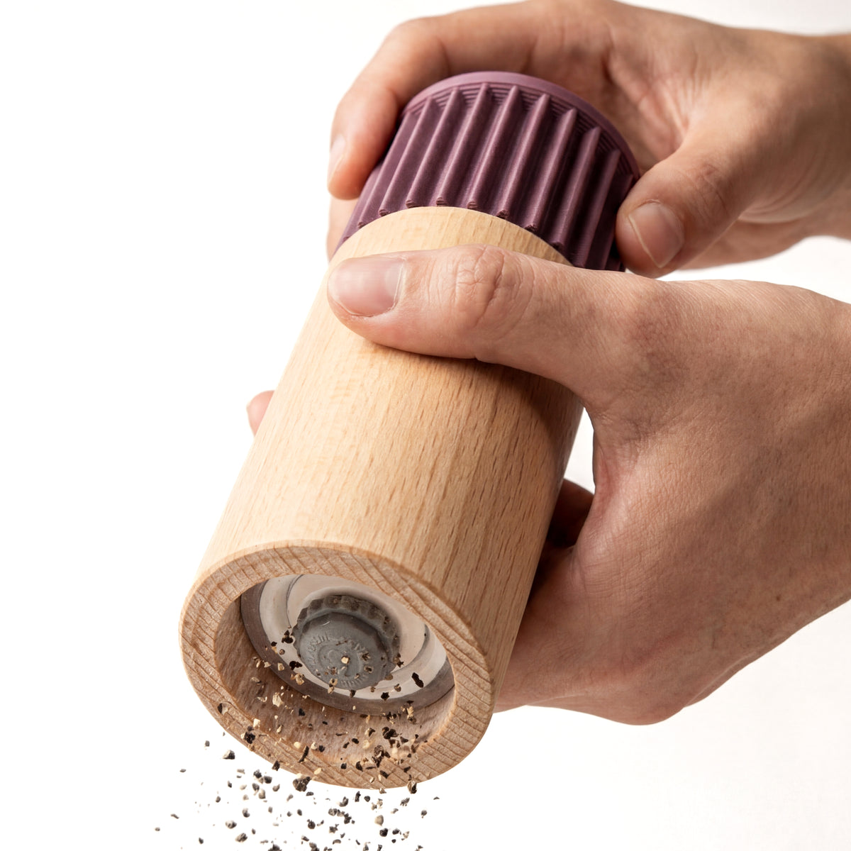 Hände mahlen Pfeffer mit der Gewürzmühle Prise in lila aus Buchenholz vor weißem Grund #farbe_aschlila