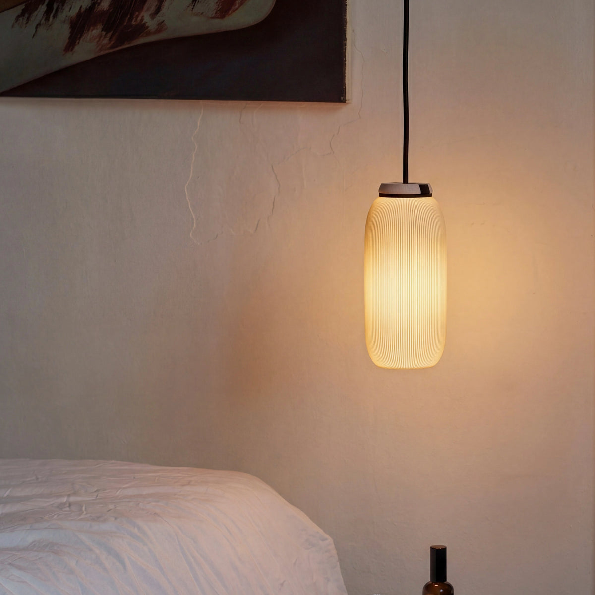 Pendelleuchte PILLE mit warmem Licht über Bett vor Lehmwand mit Kunstdruck im Schlafzimmer
